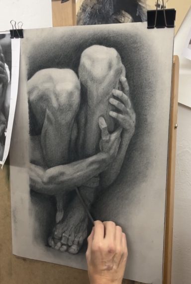 Un dibujo en carboncillo de una figura humana abrazándose a sí misma.